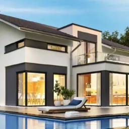 Nowoczesny dom murowany z płaskim dachem i szklaną balustradą na balkonie, widok z ogrodu z basenem.