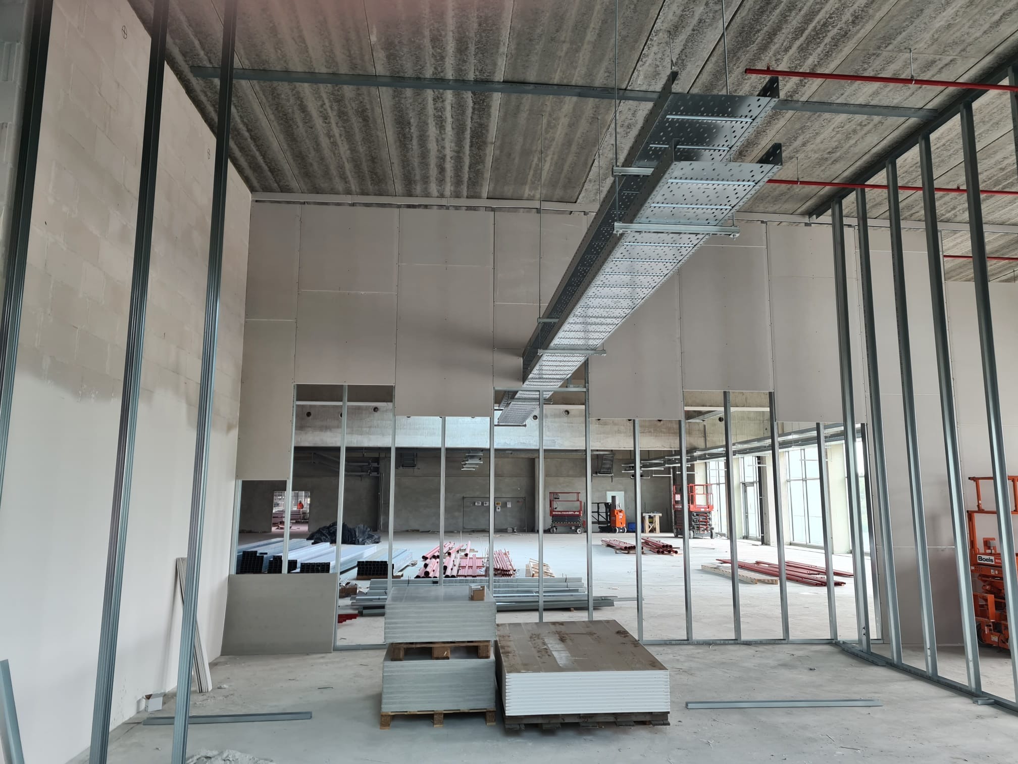 Montaż ścian działowych z płyt kartonowo-gipsowych w surowym stanie, widoczne metalowe profile i ułożone płyty na paletach.