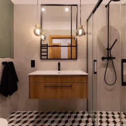 Nowoczesna łazienka z geometryczną podłogą, drewnianą szafką pod umywalką, czarną armaturą i kabiną prysznicową ze szklanymi drzwiami, oświetlona wiszącymi lampami z okrągłymi kloszami.