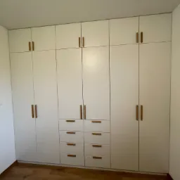 Biała szafa wnękowa z drewnianymi uchwytami, zabudowa od podłogi do sufitu, na podłodze parkiet