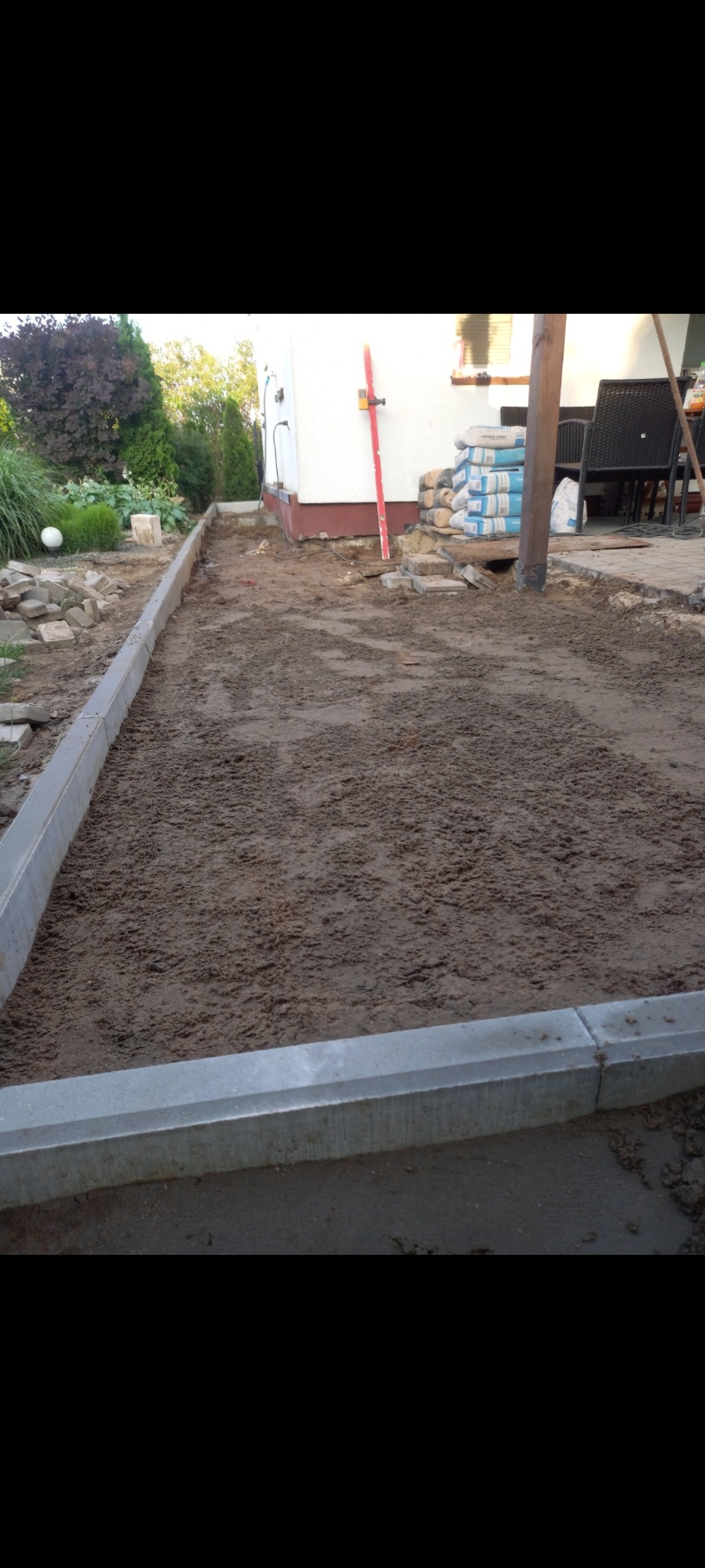 Przygotowanie podłoża pod nawierzchnię: wyrównany teren z obrzeżami, w tle worki z cementem i poziomica oparta o ścianę budynku.