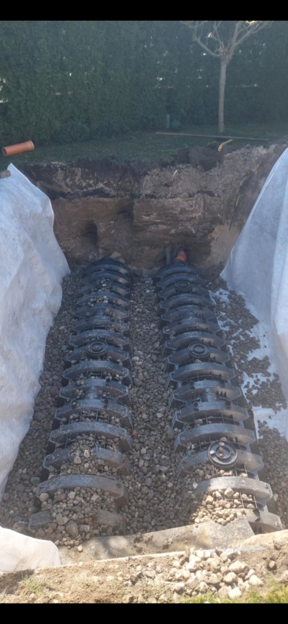 Montaż drenażu rozsączającego w Nakle nad Notecią. Widoczne tunele rozsączające obsypane żwirem, wykop zabezpieczony geowłókniną. Prace ziemne w toku.