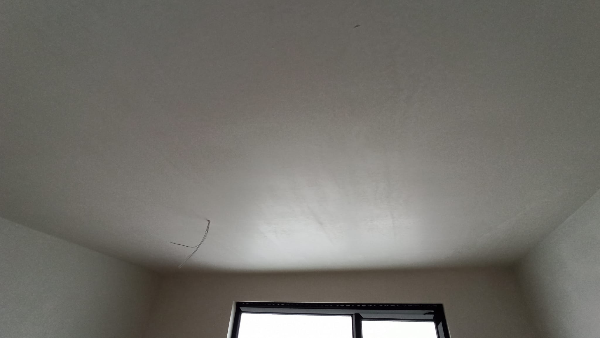 Świeżo położony, jasny tynk na suficie w pokoju z widocznym fragmentem okna i wystającym przewodem.
