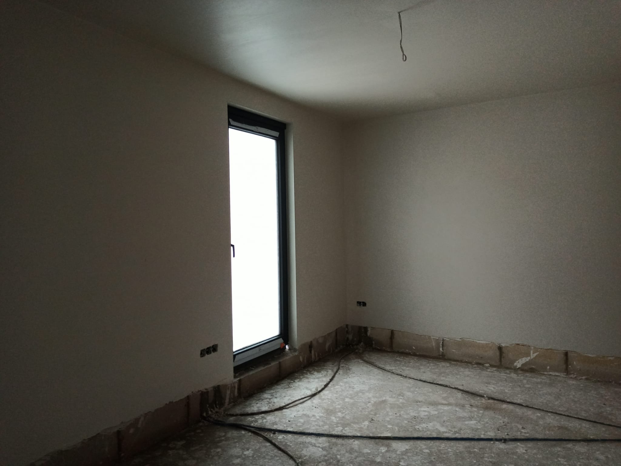 Pokój po nałożeniu gładzi szpachlowej, widoczne przewody elektryczne na podłodze i przygotowane podłoże pod listwy przypodłogowe.