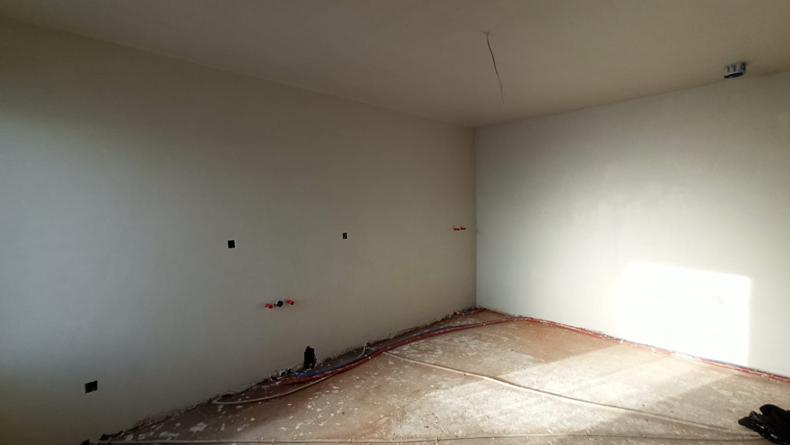 Wnętrze po nałożeniu jasnych tynków, widoczne instalacje elektryczne i hydrauliczne w podłodze, przygotowane do dalszych prac wykończeniowych.