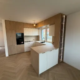 Nowoczesna kuchnia z wyspą, drewniane fronty szafek górnych i dolnych, białe szafki na wyspie, oświetlenie LED w regale, parkiet w jodełkę, czarny zlew.