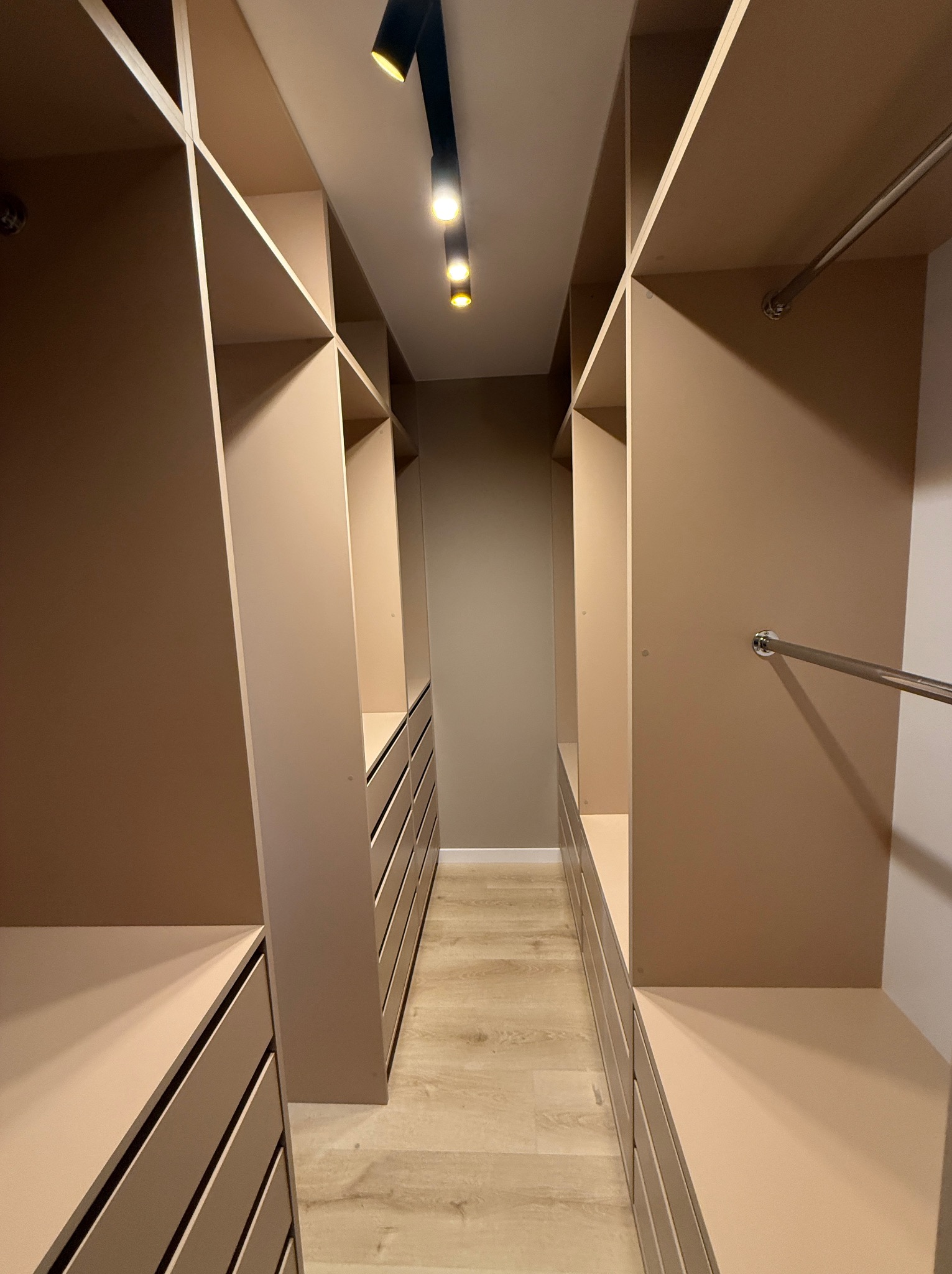 Beżowa garderoba na wymiar z oświetleniem sufitowym. Widok na wnętrze z szufladami i półkami. Minimalistyczny design.