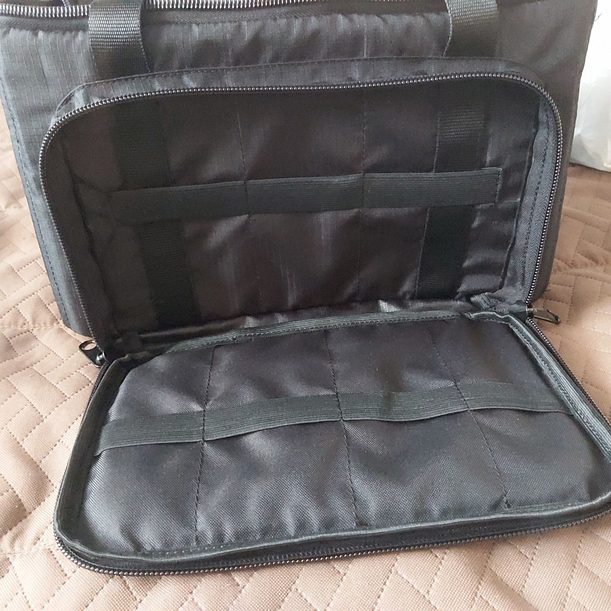 Otwarta, czarna torba z wewnętrznymi elastycznymi paskami na narzędzia lub akcesoria, leżąca na pikowanej narzucie.