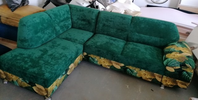 Szmaragdowy narożnik z weluru, wykończony pasem z motywem tropikalnych liści, na niskich, chromowanych nóżkach.