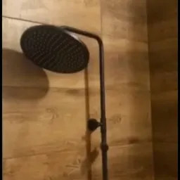 Czarna deszczownica zamontowana na ścianie wyłożonej płytkami imitującymi drewno w nowoczesnej łazience.