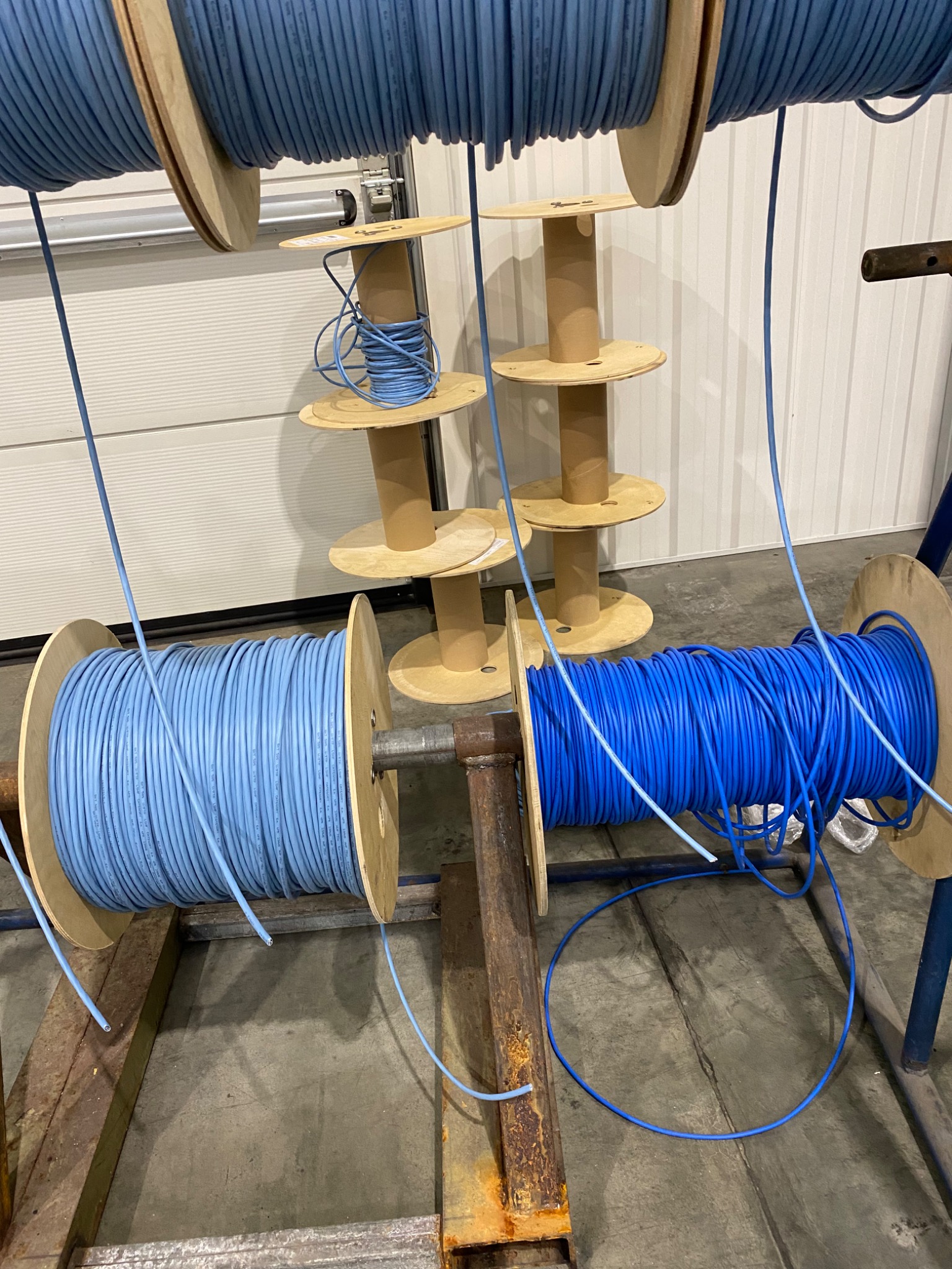 Szafa rack z nawiniętymi kablami sieciowymi w odcieniach niebieskiego na drewnianych szpulach, widok z bliska na kable wychodzące ze szpul.