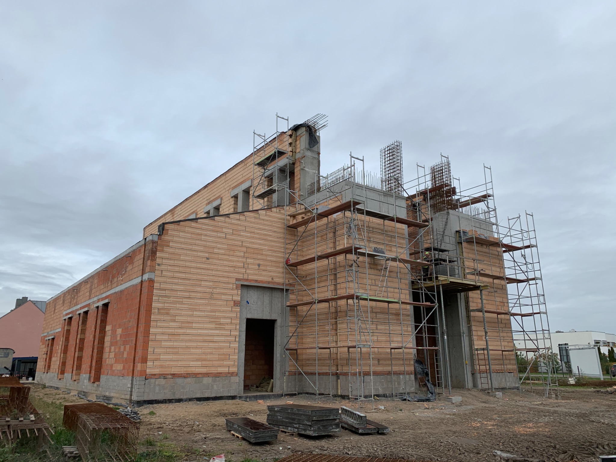 Budowa domu z cegły ceramicznej Porotherm, widoczne rusztowania i zbrojenia na dachu w pochmurny dzień.