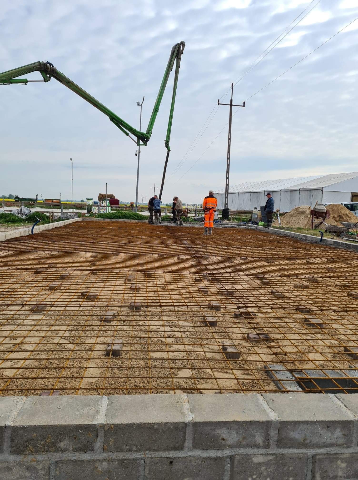 Przygotowanie zbrojenia pod wylewkę fundamentową z użyciem pompy do betonu, widoczni pracownicy w odzieży roboczej, teren budowy.