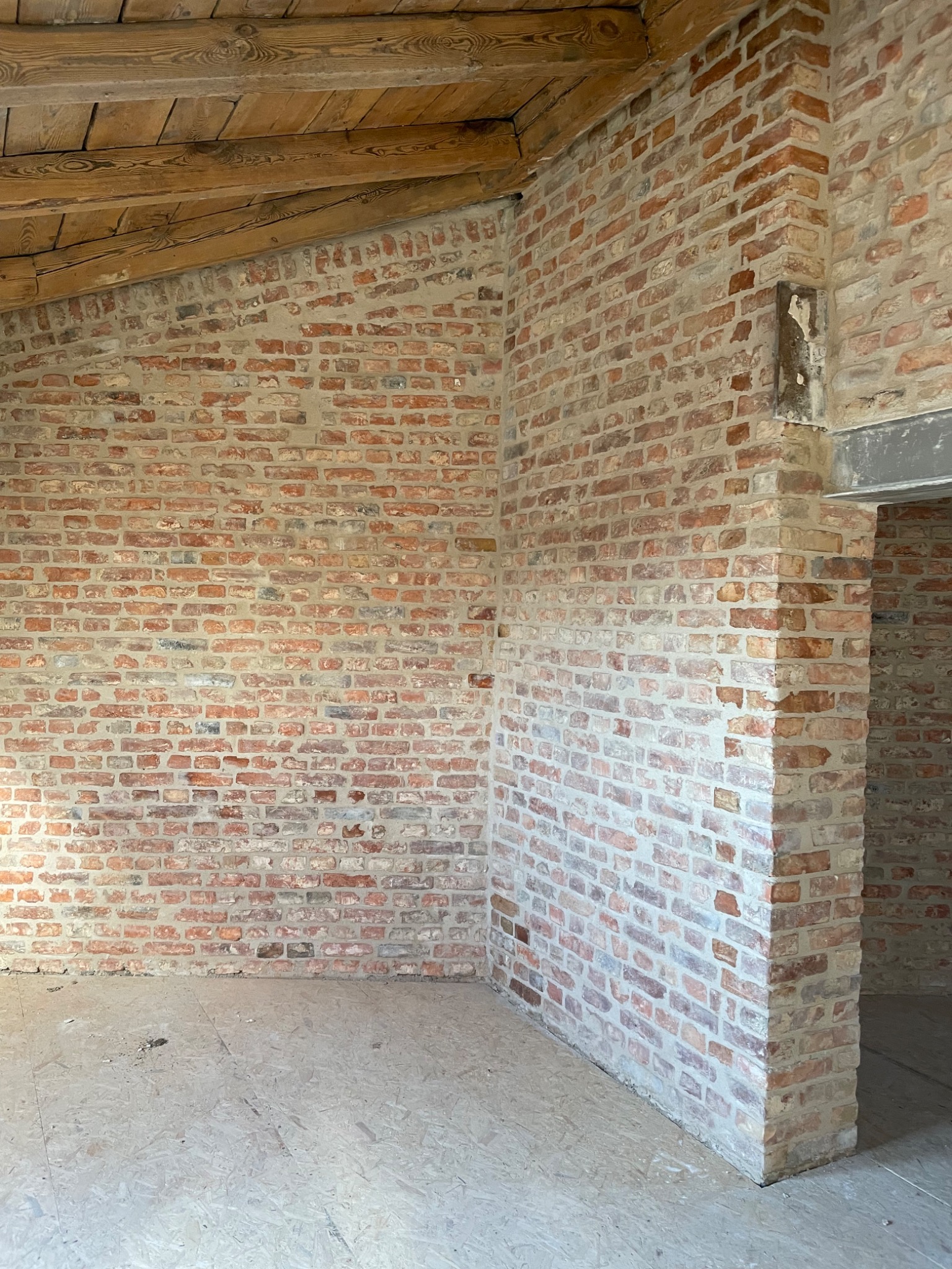 Wnętrze w trakcie budowy z czerwoną cegłą, drewnianym stropem i surową podłogą z płyty OSB.