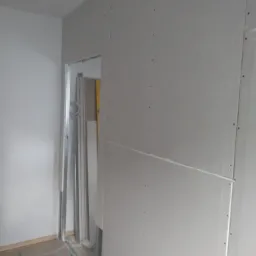 Montaż płyty karton gips w Świebodzinie, widoczne profile i fragment podłogi zabezpieczony kartonem, przygotowanie do dalszych prac wykończeniowych.