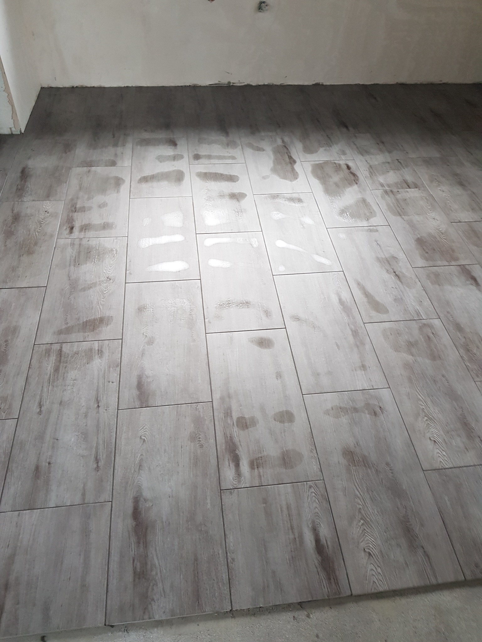 Świeżo ułożone, szare panele podłogowe imitujące drewno, z widocznymi śladami po pracy i niedoczyszczonymi fugami przy ścianach.