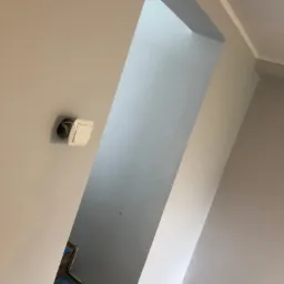 Świeżo pomalowane wnętrze z widocznym przejściem między pokojami. Na ścianie widać niedokończone gniazdko elektryczne, a podłoga zabezpieczona folią malarską.