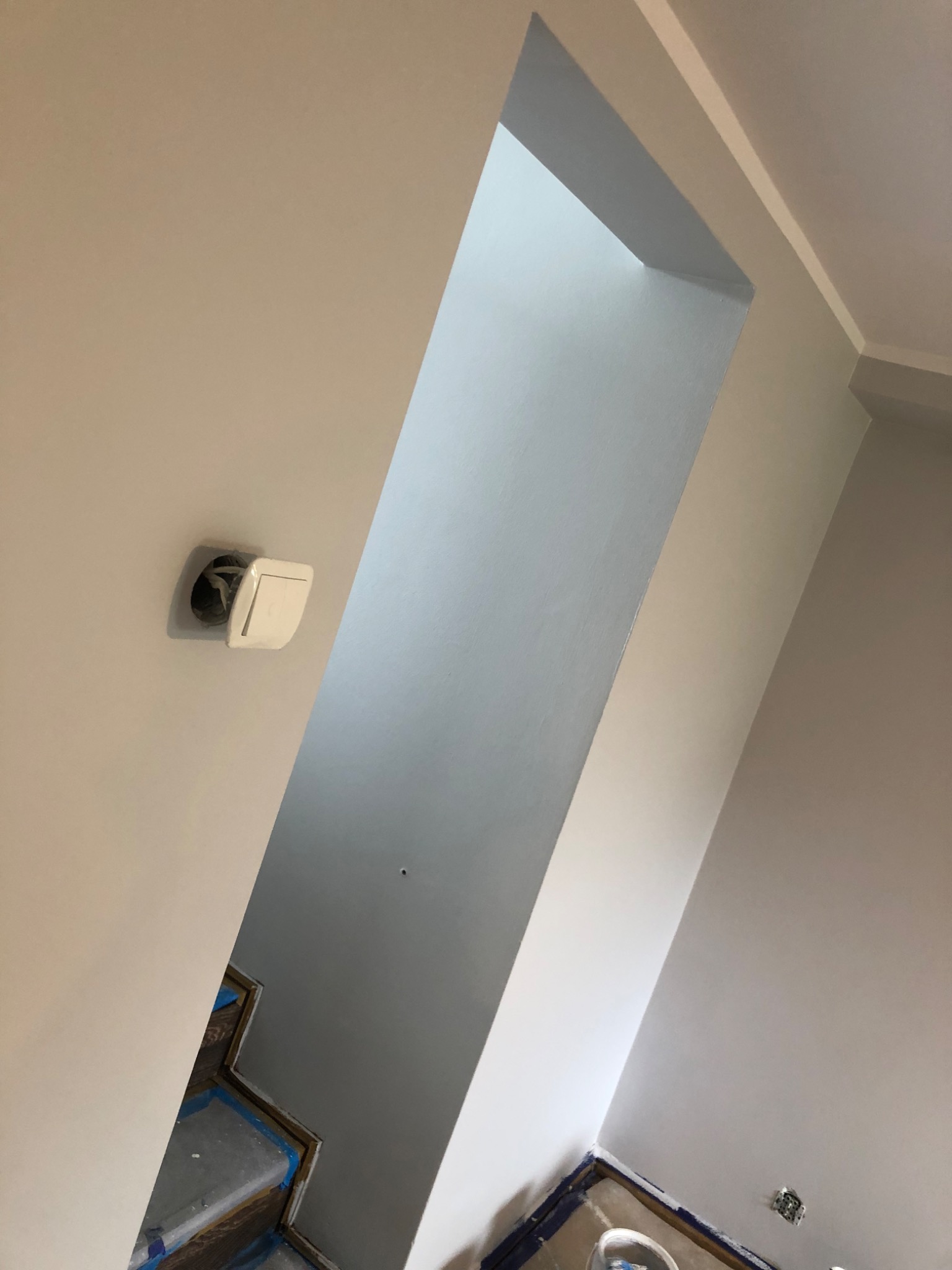 Świeżo pomalowane wnętrze z widocznym przejściem między pokojami. Na ścianie widać niedokończone gniazdko elektryczne, a podłoga zabezpieczona folią malarską.