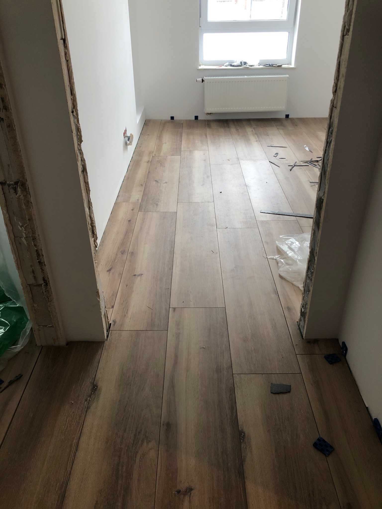 Układanie podłogi z paneli imitujących drewno w trakcie remontu w Suwałkach, widoczne kliny dystansowe i resztki po cięciu paneli.