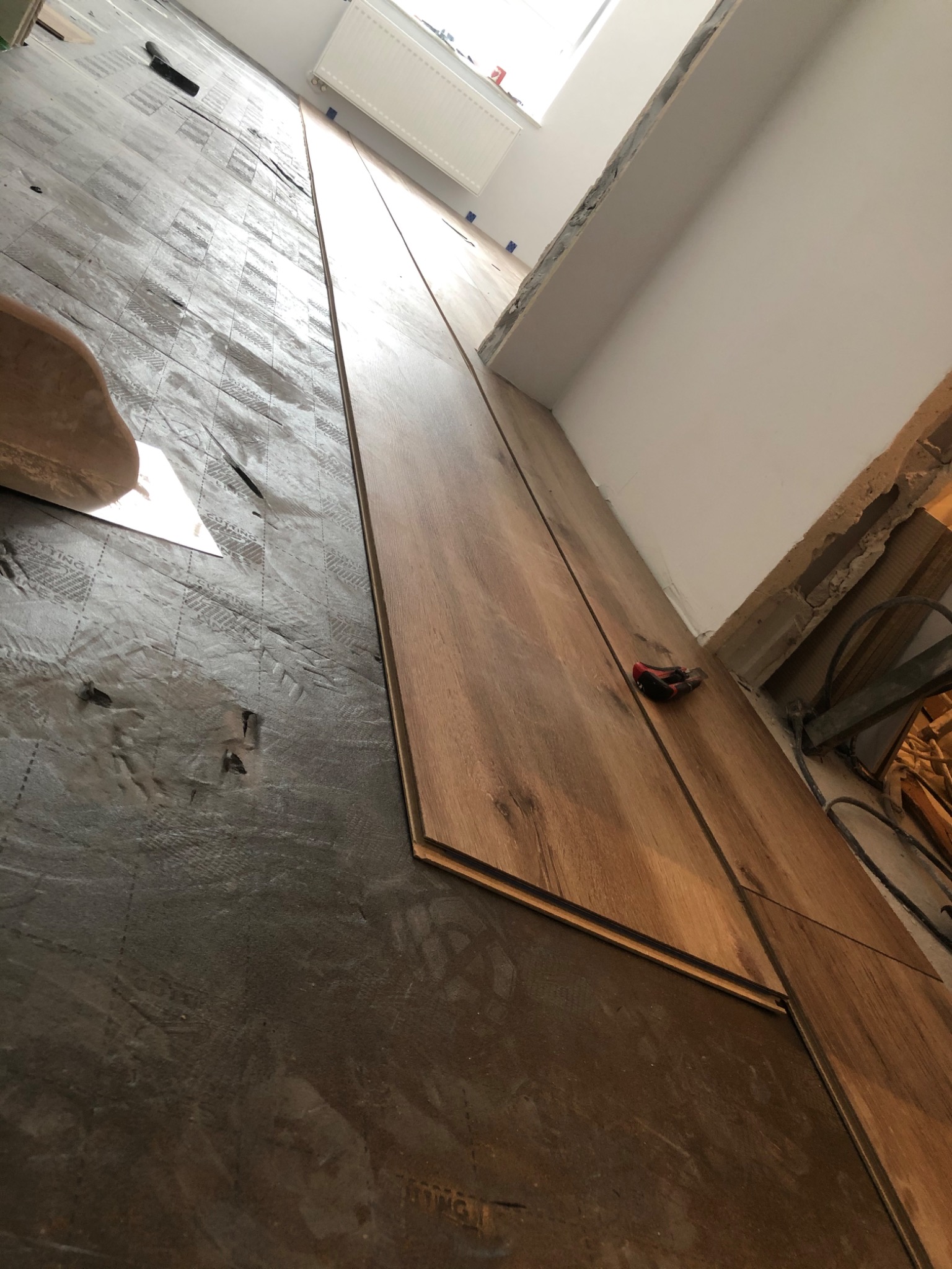 Montaż paneli podłogowych na podkładzie izolacyjnym, widoczny nożyk do tapet przy ścianie.