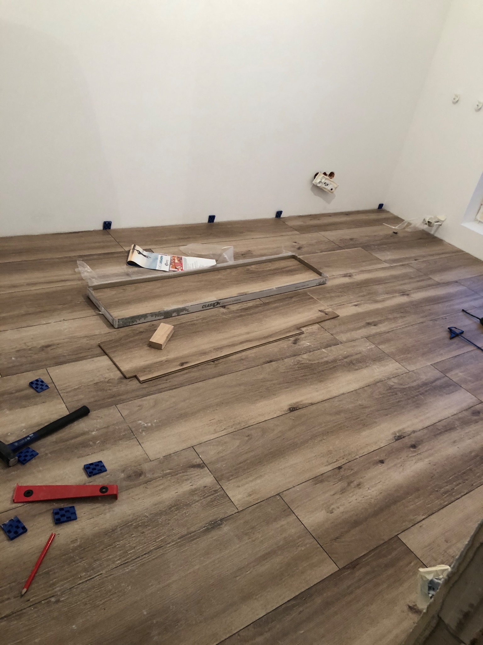 Układanie podłogi z płytek imitujących drewno w trakcie remontu, widoczne narzędzia glazurnicze, paczka płytek i krzyżyki dystansowe.