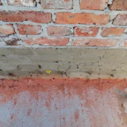 Ceglany fundament z widocznymi śladami wilgoci i zamocowanymi kołkami montażowymi, przygotowany do dalszych prac zabezpieczających.