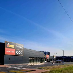 MARPAP - Nowoczesna hala handlowa z czarną elewacją z płyt warstwowych i logo Biedronka, Martes Sport i CCC, widziana z perspektywy ulicy w słoneczny dzień.