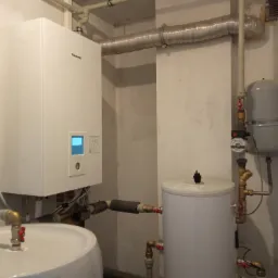 Biały wiszący piec grzewczy Panasonic z wyświetlaczem i zbiornikami na wodę, rurami i zaworami w piwnicy.