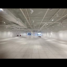 GEFEST IVAN BRAZHNYK - Duża, pusta przestrzeń biurowa z białymi ścianami, podłogą z płytek i metalową konstrukcją sufitową z oświetleniem punktowym. Dwóch pracowników w oddali, przygotowujących podłoże. Świeżo wykończone...