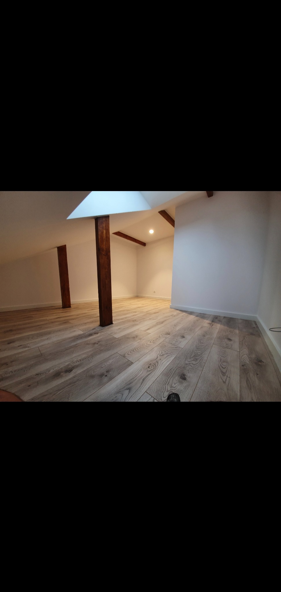 Poddasze po remoncie z drewnianymi belkami, jasnymi panelami podłogowymi i oknem dachowym.