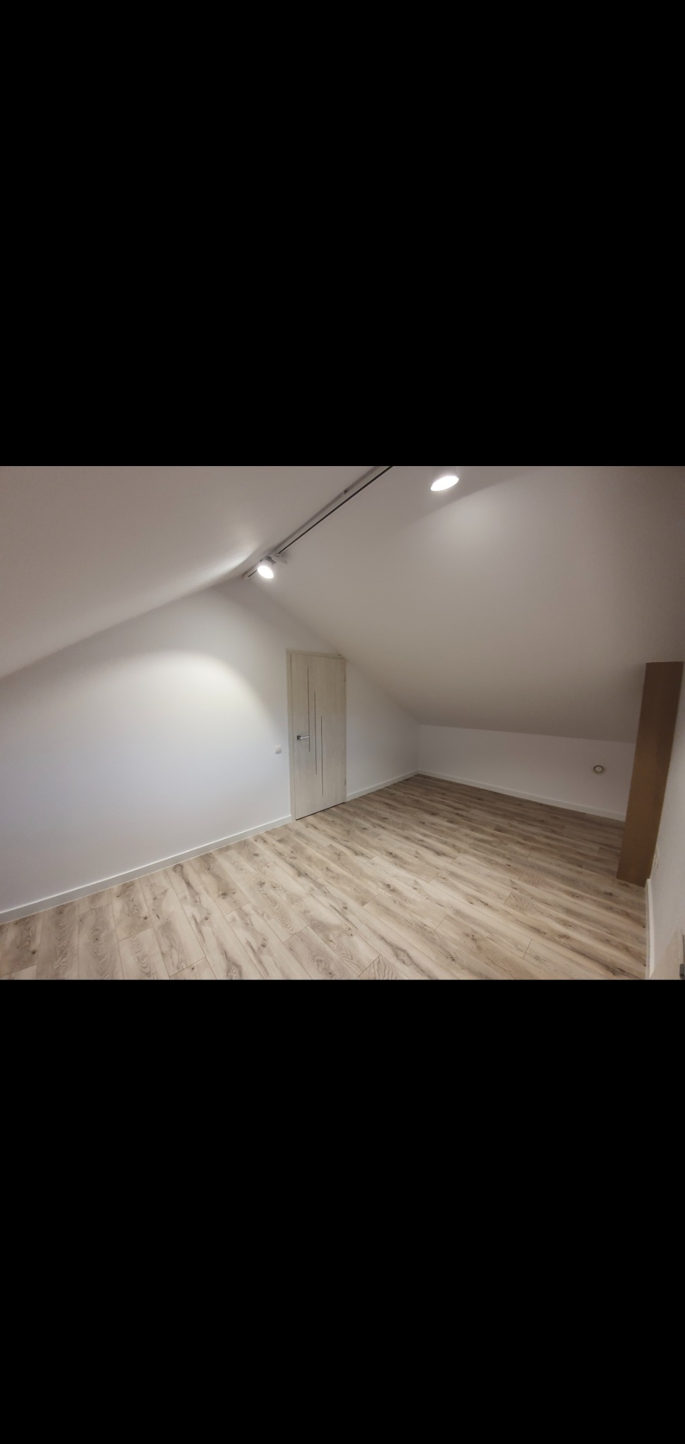 Poddasze po remoncie z jasną podłogą imitującą drewno, białe ściany i zamontowane oświetlenie punktowe na szynie.