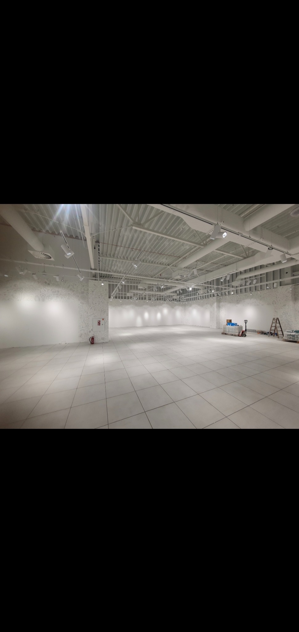 Wnętrze biurowe w Markach, przygotowane do malowania, widoczne białe ściany, podłoga wyłożona płytkami, sufit z instalacjami, drabina i materiały budowlane w rogu.