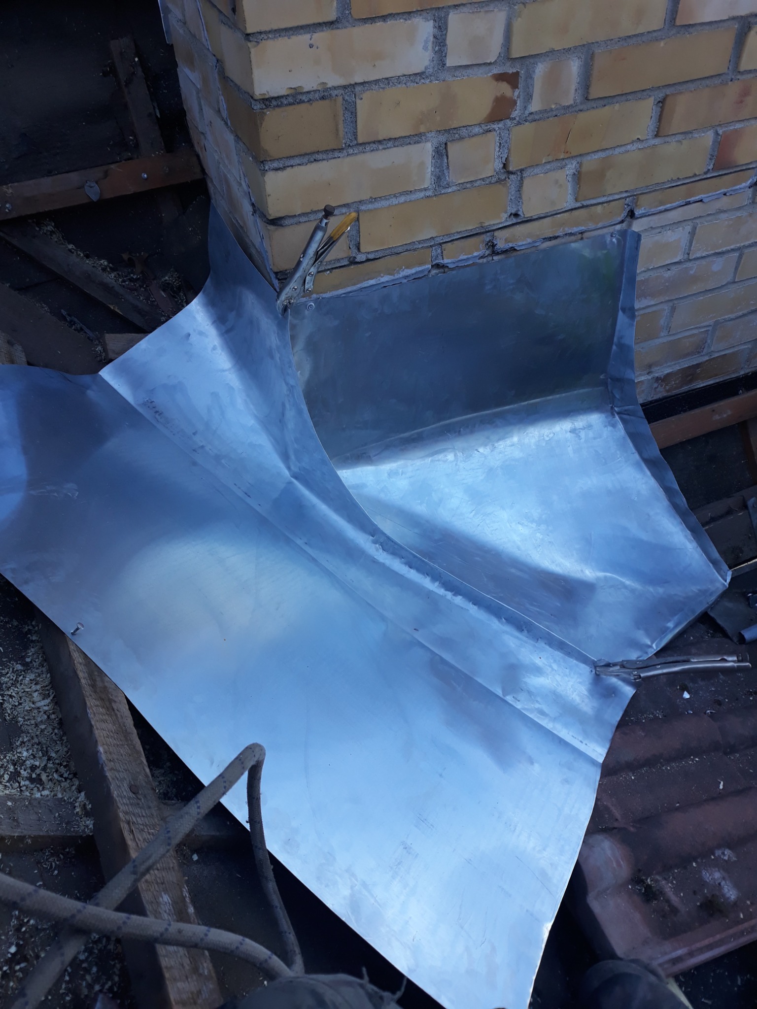 Blacha opierzenia komina dachowego mocowana zaciskami do cegieł, widoczne elementy konstrukcji dachu.