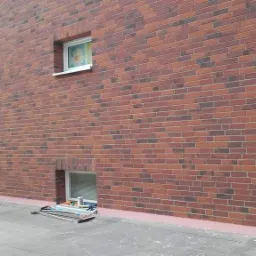 Ceglana elewacja budynku po renowacji w Złotoryi, widoczne rusztowanie i narzędzia pracy.