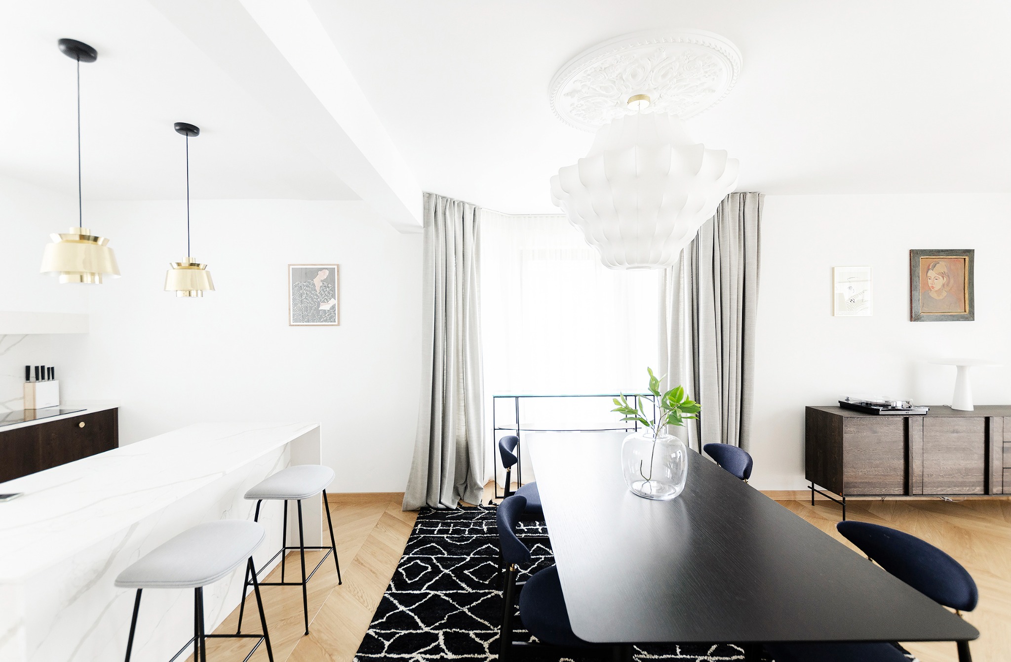 Jasne wnętrze z czarnym, minimalistycznym stołem, marmurowym blatem kuchennym i designerskimi lampami wiszącymi w stylu skandynawskim.