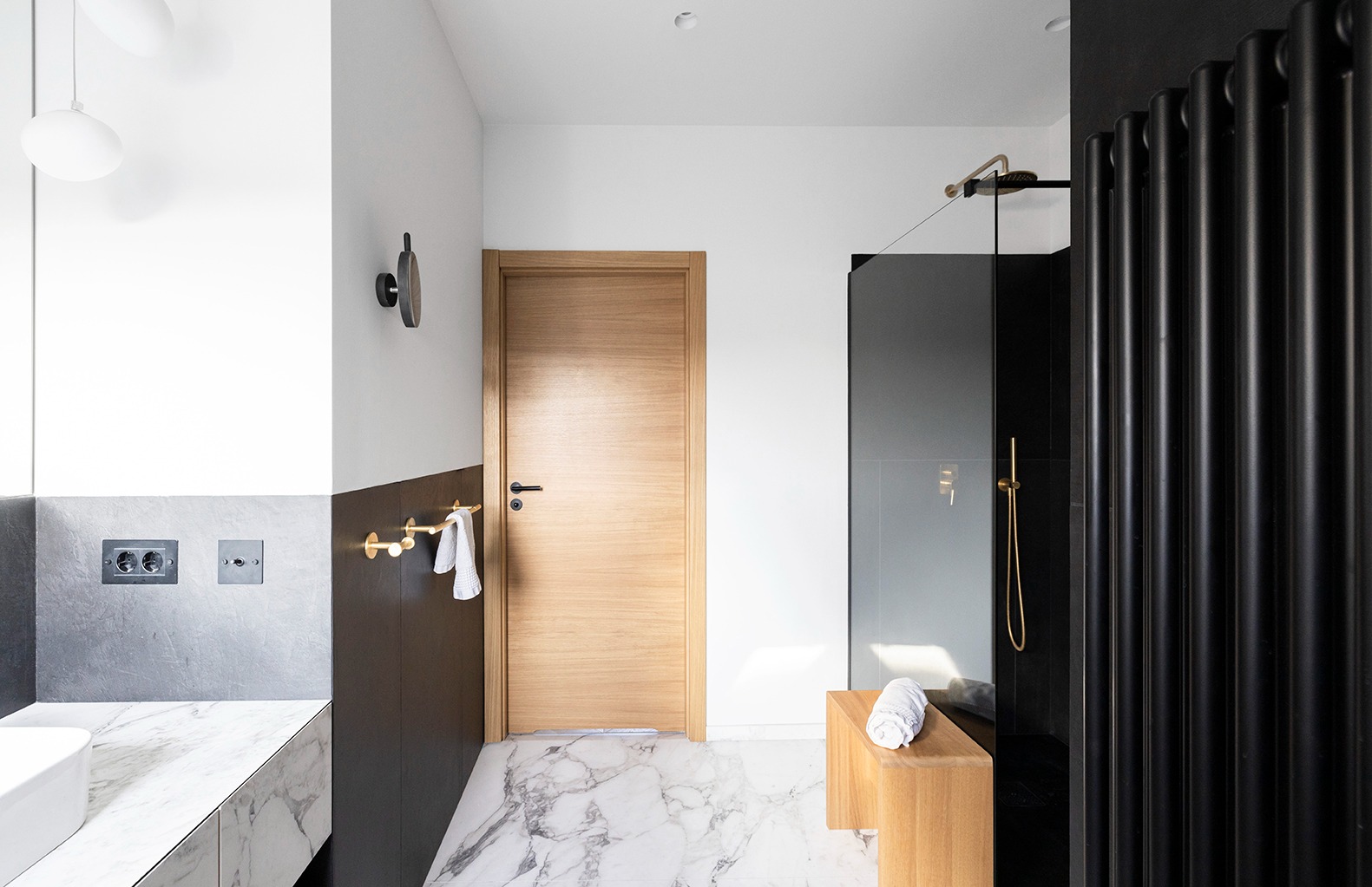 Nowoczesna łazienka z marmurową podłogą, drewnianymi akcentami, czarną kabiną prysznicową i grzejnikiem żeberkowym.