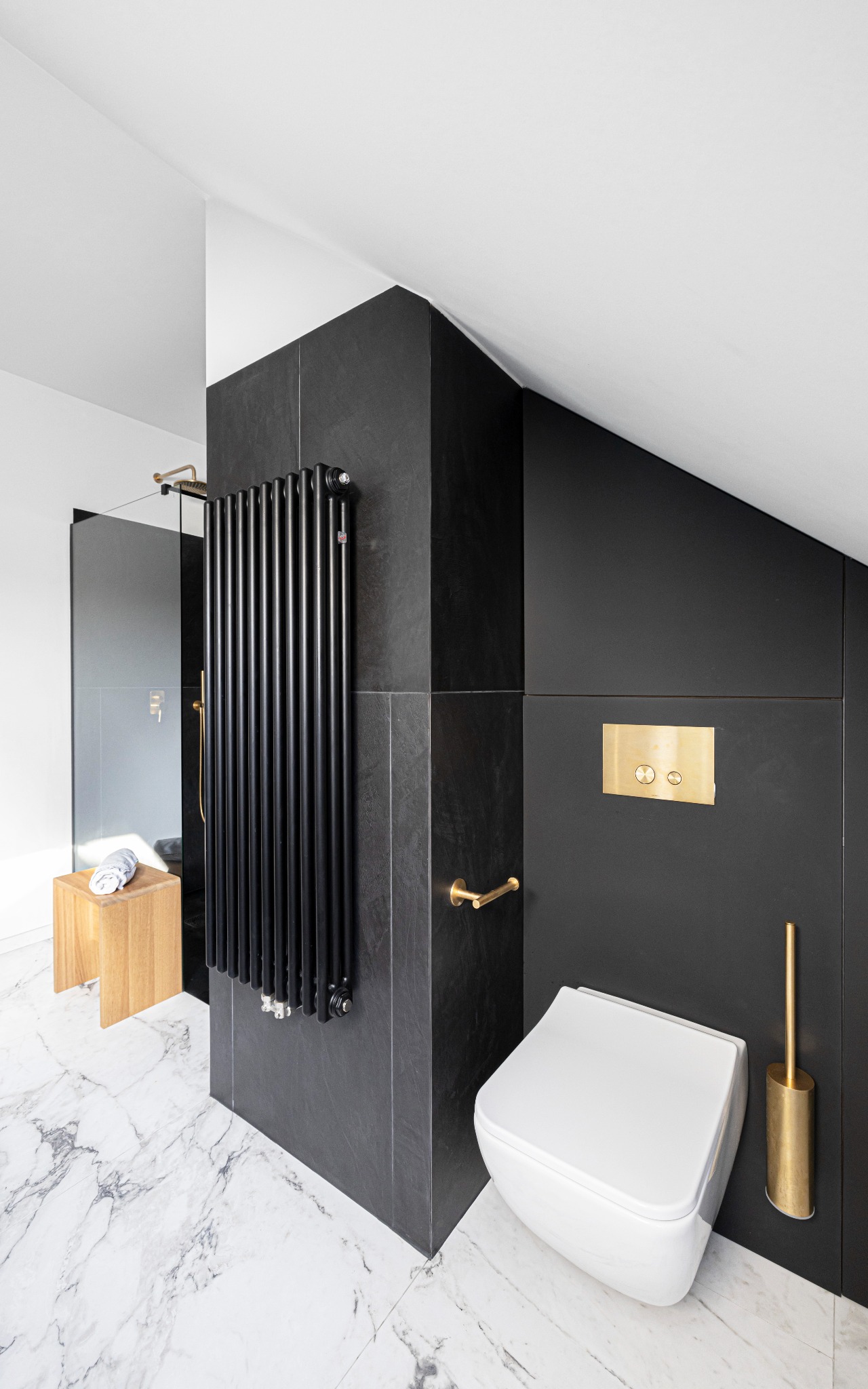 Nowoczesna łazienka w czerni i bieli z marmurową podłogą, czarnymi płytkami ściennymi, białym wiszącym sedesem i złotymi akcentami, takimi jak szczotka do WC i bateria.