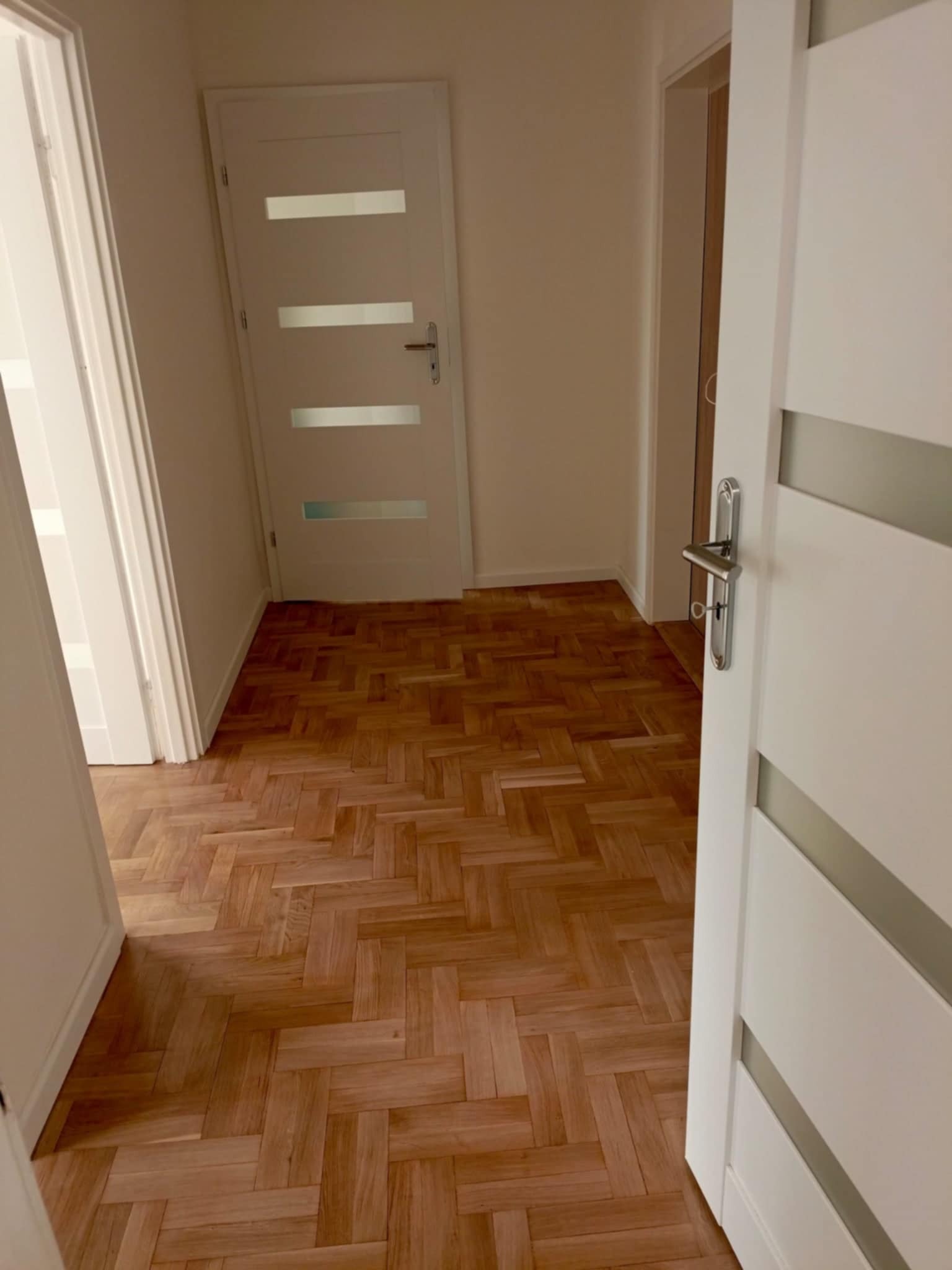 Parkiet ułożony w jodełkę w jasnym korytarzu z białymi drzwiami z przeszkleniami.