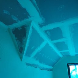 Anar Vasetskyi - Niedokończona sufitowa konstrukcja z płyt gipsowo-kartonowych, widoczne łączenia i fragmenty niezagruntowanej powierzchni, oświetlenie budowlane w tle.