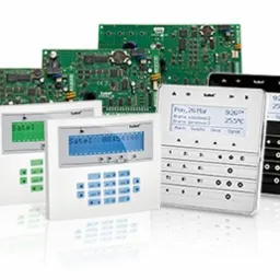 Zestaw urządzeń alarmowych firmy Satel: centrale alarmowe z widocznymi płytami głównymi, białe manipulatory z wyświetlaczami LCD (zielony, niebieski, biały) oraz czarny manipulator dotykowy.