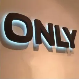 Podświetlany napis 'ONLY' z ciemnobrązowych, trójwymiarowych liter zamontowany na jasnej ścianie, z efektem halo tworzonym przez białe światło LED za literami.