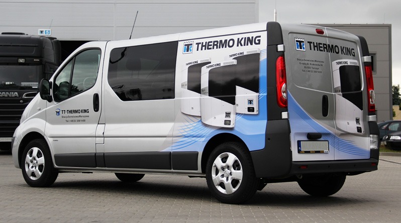 Srebrny van z grafiką reklamową chłodni Thermo King, zaparkowany na zewnątrz budynku, z widocznymi elementami identyfikacji wizualnej firmy.