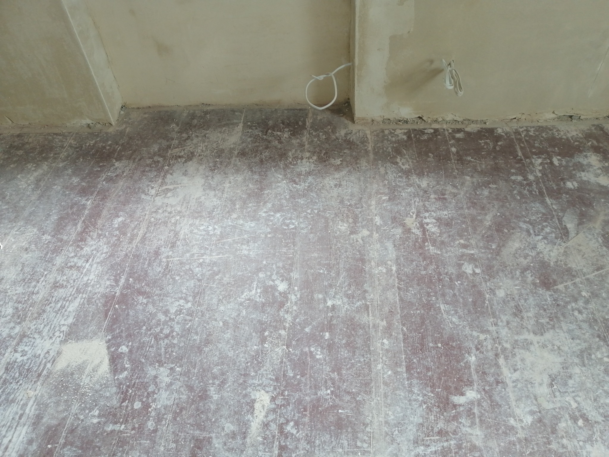 Podłoga parkietowa pokryta pyłem po cyklinowaniu, widoczne wystające kable elektryczne ze ściany, ściany w trakcie wykończenia gipsowego.