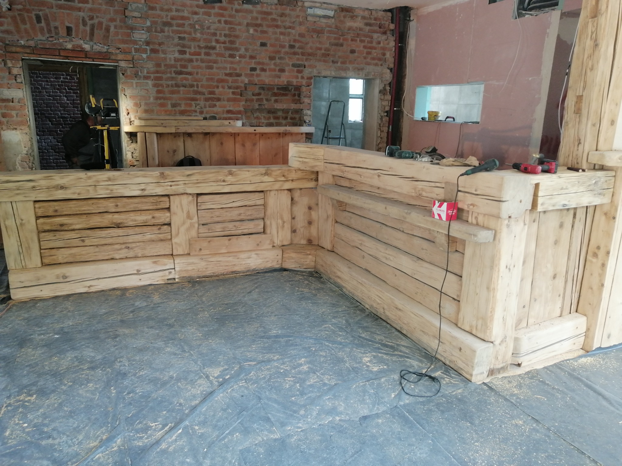 Surowa drewniana konstrukcja baru z bali w trakcie montażu w Jeleniej Górze, widoczne narzędzia i niezabezpieczona podłoga.