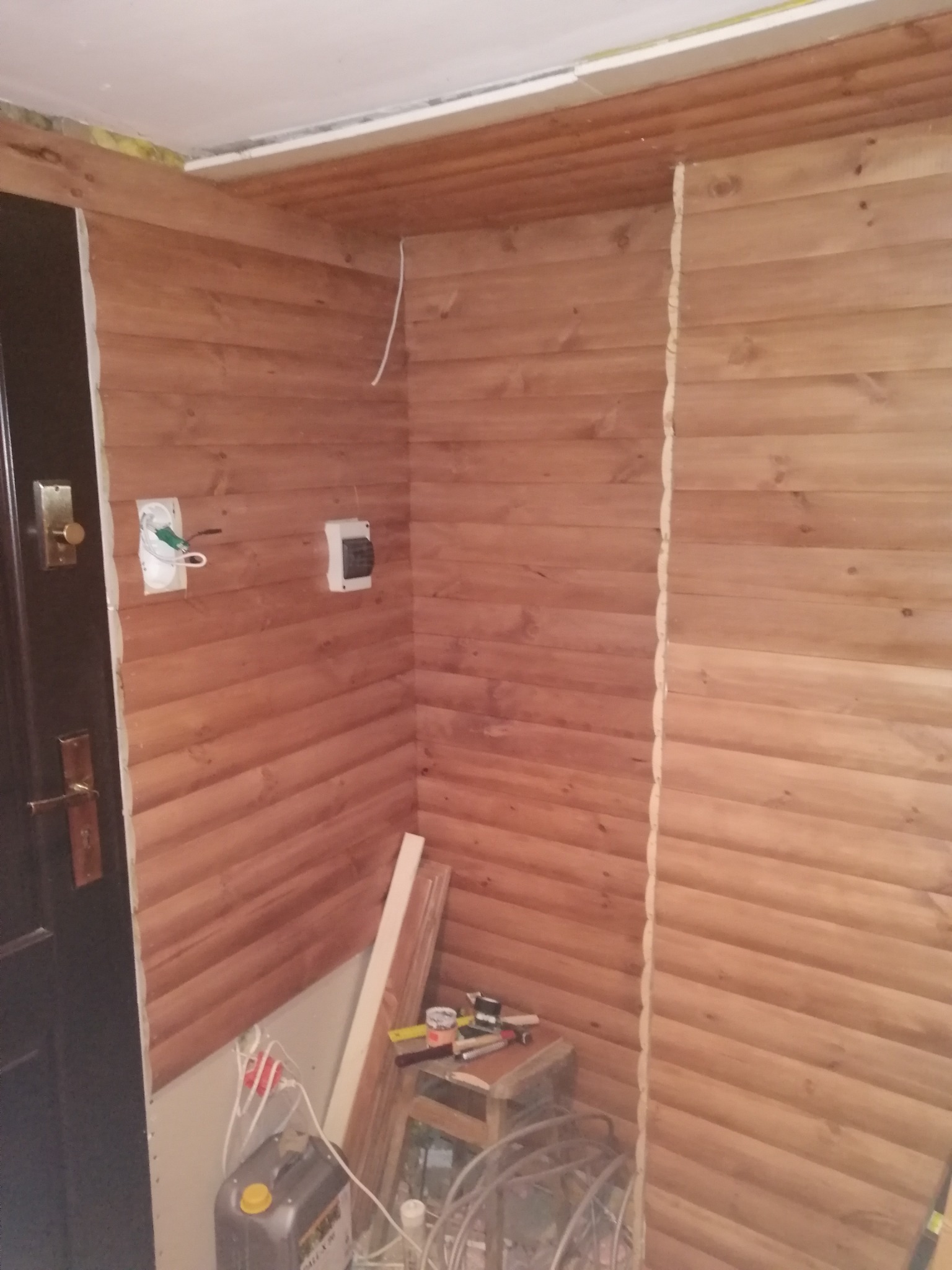 Wnętrze w trakcie montażu boazerii drewnianej, widoczne puszki elektryczne i narzędzia.
