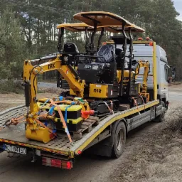 Dwie mini koparki NEX N12 zabezpieczone pasami na platformie lawety, widok z tyłu, tablica rejestracyjna WOT 84150.