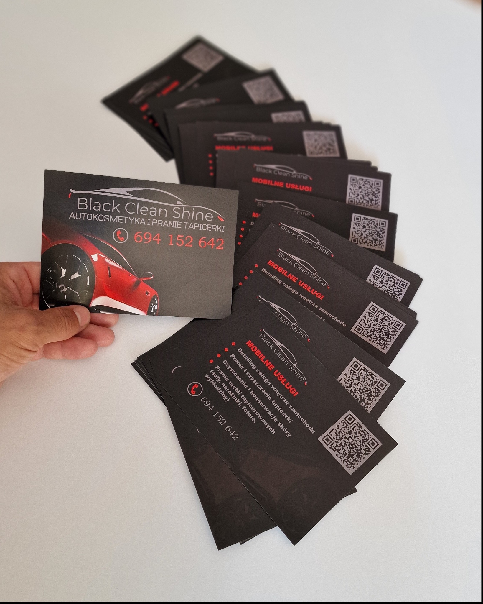 Stos wizytówek firmy Black Clean Shine oferującej autokosmetykę i pranie tapicerki, z widocznym logo i numerem telefonu.