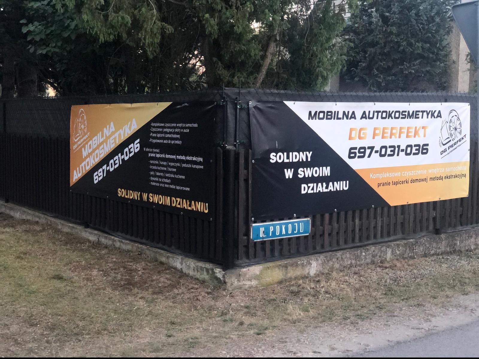 Dwa banery reklamowe firmy 'Mobilna Autokosmetyka DG Perfekt' zawieszone na ogrodzeniu, oferujące kompleksowe czyszczenie wnętrz samochodów oraz pranie tapicerki domową metodą ekstrakcyjną...