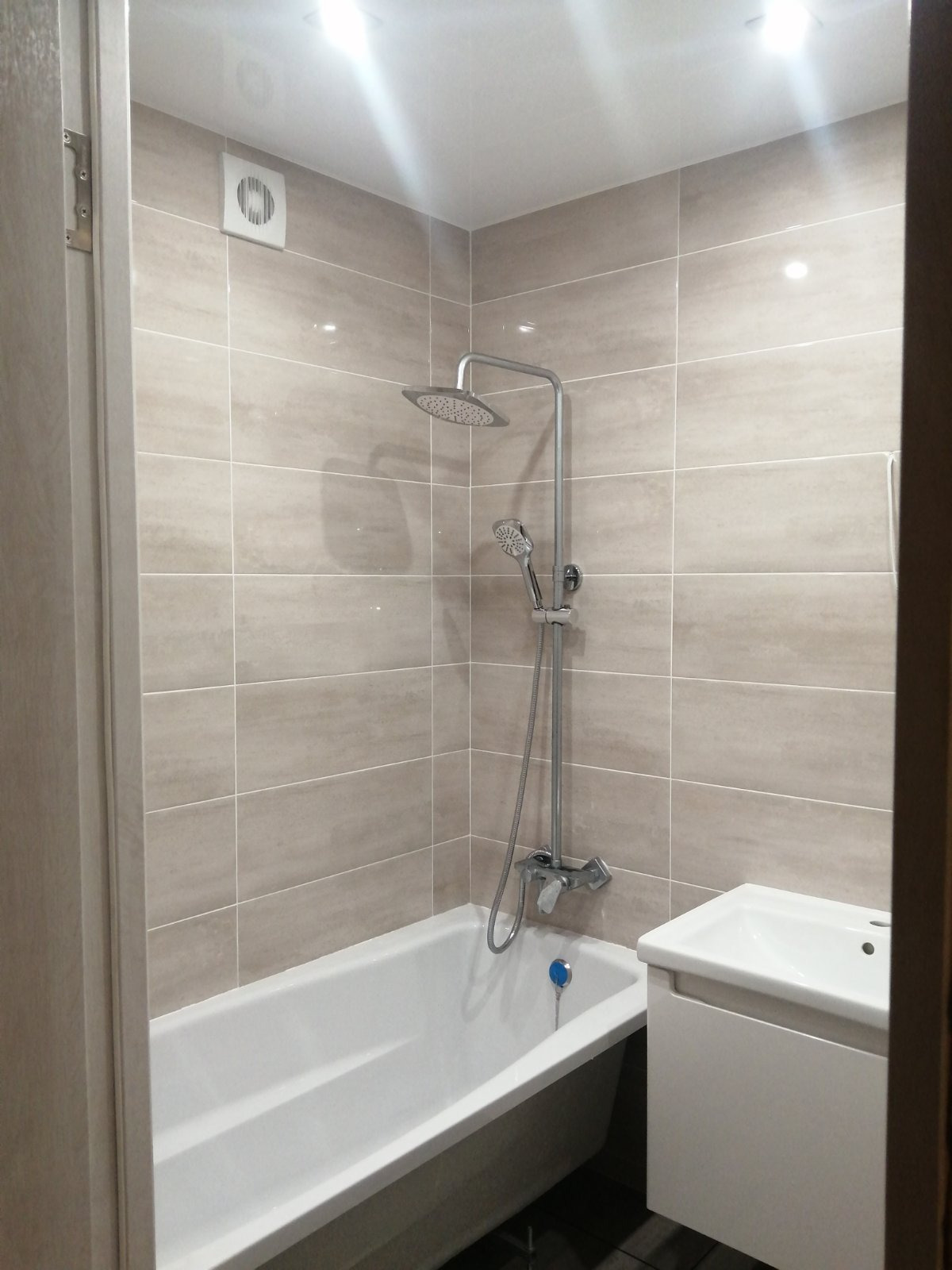 Wykończona łazienka w Opolu z beżowymi płytkami, białą wanną i umywalką w szafce. Widoczny zestaw prysznicowy z deszczownicą i wentylator sufitowy.