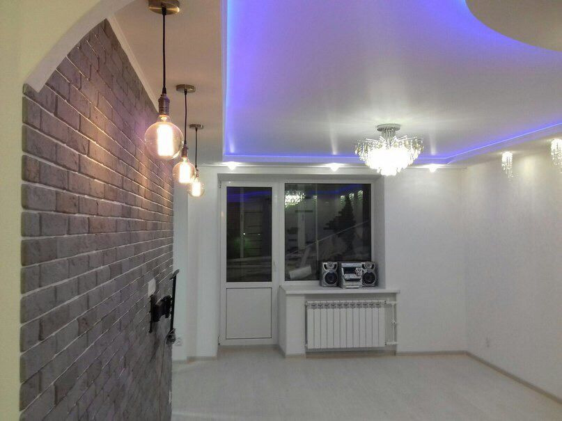 Pokój po odświeżeniu z dekoracyjną ścianą z cegły, trzema wiszącymi lampami Edison, kryształowym żyrandolem i podświetlanym sufitem w kolorze niebieskim.